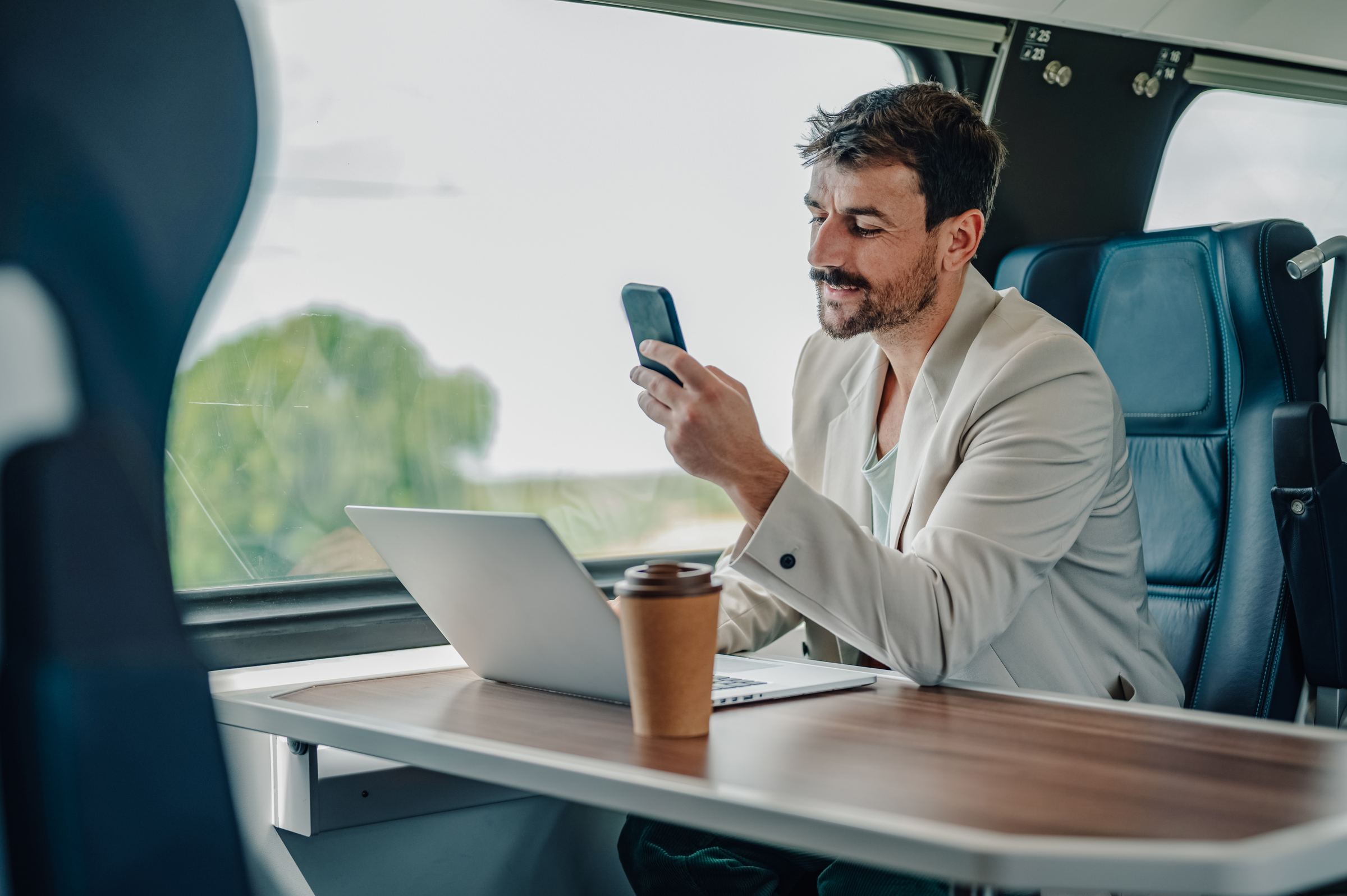 Business owner checking his phone while working on a laptop during a train commute